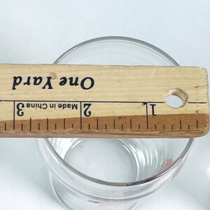 May include: A clear glass tumbler with a wooden ruler placed across the top. The ruler is marked with inches and the text "One Yard" and "Made in China". The tumbler is on a white surface.