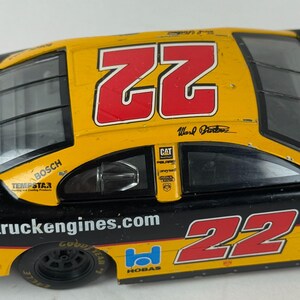 May include: A yellow and black race car model with the number "22" in red. The car features sponsor logos including "BOSCH", "CAT", and "truckengines.com". The car has black tires and windows.