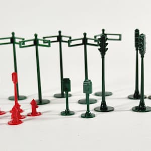 May include: Miniature green street signs, traffic lights, and mailboxes, along with red fire hydrants and street lamps. These small-scale models are likely for a model train set or diorama, offering a detailed urban landscape.