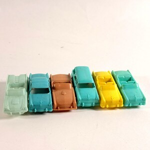 May include: A collection of six small plastic toy cars arranged in a row. The vehicles include a pale green convertible, a bright blue sedan, a peach-colored coupe, a teal station wagon, a yellow convertible, and a light green convertible.