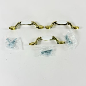 May include: Set of four cabinet pulls with a gold finish and white ceramic center. Each pull is accompanied by a small packet of screws. The pulls have a classic, elegant design, suitable for kitchen or bathroom cabinetry.