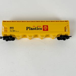 May include: A yellow model train car with black wheels. The car has the words "Shell Chemical Plastics" printed on the side, along with the Shell logo and other text.