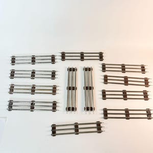 May include: A collection of twelve metal model train track sections. Ten sections are arranged horizontally in two columns, while two sections are positioned vertically in the center. Each track piece features three parallel rails.
