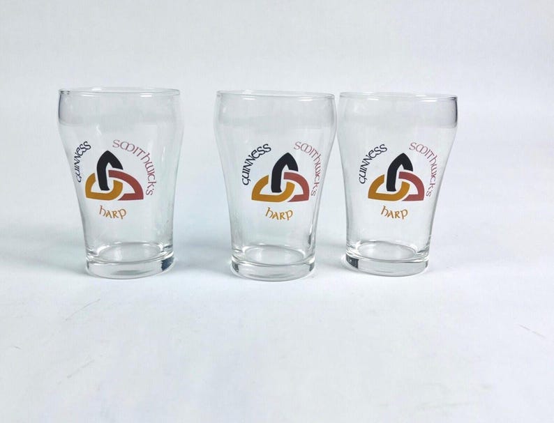 May include: Three clear pint glasses, each bearing the Guinness logo with a harp design and the words "SCOTTUCKS" and "HARP". The glasses are empty and stand on a white surface.