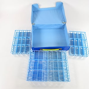 May include: A light blue suitcase with a matching interior and several removable blue plastic trays. The suitcase has a yellow handle and metal hinges. The trays are divided into multiple compartments.