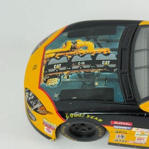 May include: A detailed close-up of a toy race car. The car is primarily yellow and black, with the words "Good Year" on the tire. The hood features a graphic of an engine with the "CAT" logo. Additional logos and text are visible on the car's body.