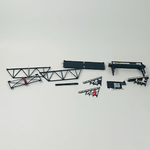 May include: A set of black plastic model train bridge pieces. The set includes two bridge supports, two bridge decks, two bridge railings, and a stop sign. The pieces are designed to be assembled to create a bridge for a model train layout.