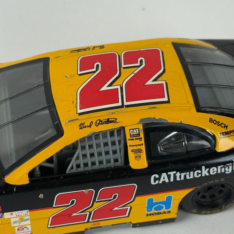May include: A yellow and black race car toy with the number 22 in red. The car has sponsor logos including CAT, Polaris, and Bosch. The text "Ward Burton" is visible on the side of the car.