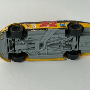May include: A yellow and black toy race car with the number 22 in red. The underside of the car is visible, showing the chassis and wheels. The car has sponsor logos and is a collectible item.