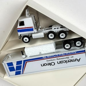 May include: A white and blue toy semi-truck with the words "American Olean" on the trailer. The truck is in a white box. The cab has a red and blue stripe design.