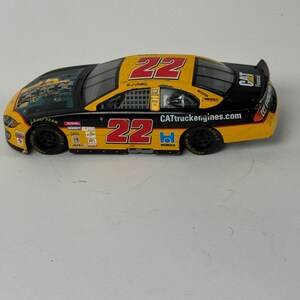 May include: A die-cast model race car with a yellow, black, and red color scheme. The number "22" is prominently displayed on the roof and sides. The car features sponsor logos and the text "CATtruckengines.com".