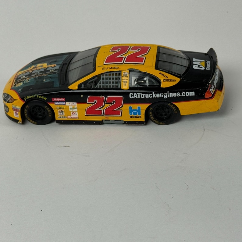 May include: A die-cast model race car with a yellow, black, and red color scheme. The number "22" is prominently displayed on the roof and sides. The car features sponsor logos and the text "CATtruckengines.com".