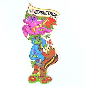 May include: A colorful HersheyPark Furry Tales sticker featuring cartoon characters Violet, Dutch, and Chip. Violet, a purple squirrel, holds a banner that reads "HersheyPark". Dutch, a blue bear, and Chip, a brown chipmunk, are also featured.