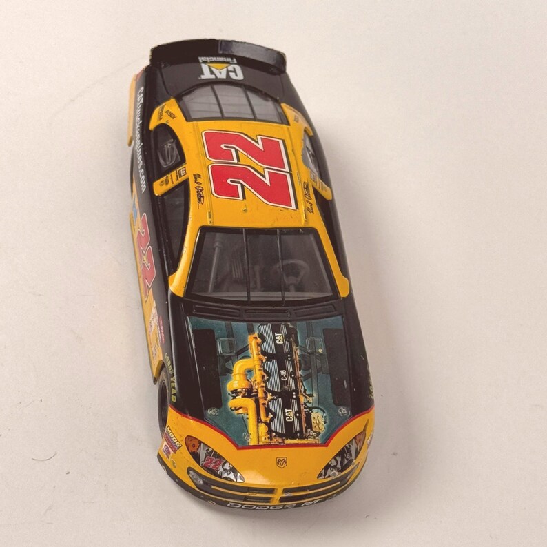 May include: A yellow and black toy race car with the number 22 in red. The car has the CAT logo and other sponsor decals. The hood shows an engine graphic. The car is a Dodge model.
