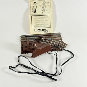 May include: A vintage Lionel train set, featuring brown track pieces, a control box, and a black wire. An instruction sheet is visible, with the Lionel logo. The set appears to be in good condition, suitable for collectors or hobbyists.