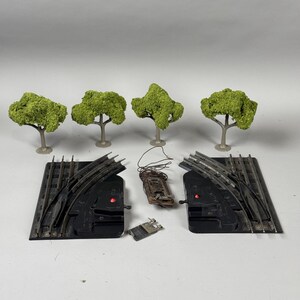 May include: A set of model train track pieces with two switches, a small wooden structure, and four green model trees. The track pieces are black plastic with silver metal rails.