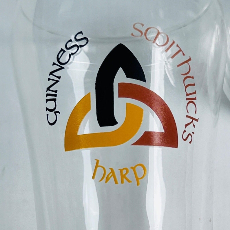 May include: A clear glass featuring the Guinness, Smithwick's, and harp logos. The logos are in black, orange, and red. The harp logo is in a stylized font. The Guinness logo is in a curved font.