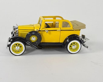 以下が含まれることがあります： 黄色と黒のコンバーチブル型ミニカー。側面にはスペアタイヤが取り付けられ、ホワイトウォールタイヤを装着しています。車内は細部まで作り込まれており、フロントグリルにはクローム調のアクセント、屋根はベージュ色で折りたたまれた状態です。