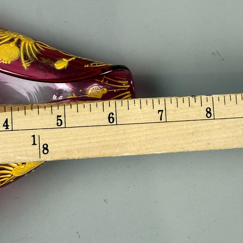 May include: A pink glass dish with gold floral designs. The dish is approximately 6 inches long.