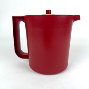 May include: A red plastic pitcher with a white lid and a handle. The pitcher is designed for serving beverages.