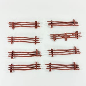 May include: Eight miniature brown wooden fences arranged on a white surface. Each fence has horizontal rails supported by vertical posts. The fences vary slightly in design, with some having a more rustic appearance.