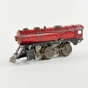 May include: A vintage red toy train with black and silver accents. The train features a detailed design with visible wear and tear, suggesting its age. The toy train has multiple wheels and a classic locomotive shape.