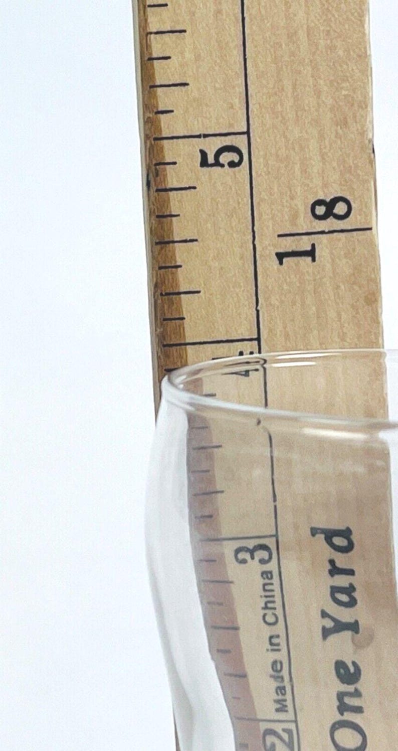 May include: A clear glass with a wooden ruler measuring 13 cm. The ruler is made of light brown wood with black markings. The glass is partially visible, with the text "Made in China" and "One Yard" printed on it.