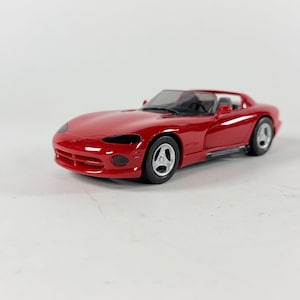 May include: A white ceramic mug with a black handle and the text "But First, Coffee" in a black, handwritten-style font. The mug is on a white surface.