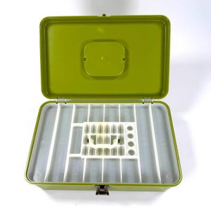 May include: Open green metal storage box with a hinged lid and a white plastic interior divided into compartments. The box has a metal clasp closure and is designed for organizing small items.