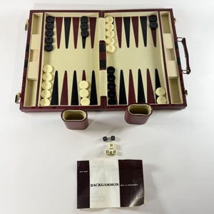 May include: A burgundy backgammon set featuring a folding board with cream-colored felt interior, black and maroon triangular points, and cream and black checkers. Includes two dice cups, two black dice, two cream dice, a doubling cube, and a rule booklet.