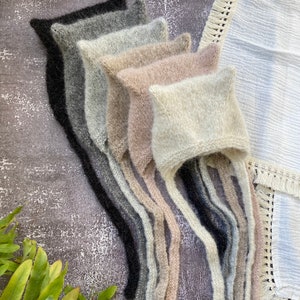 Może przedstawiać: Zestaw siedmiu dzianych czapek dla niemowląt w różnych odcieniach szarości, beżu i bieli. Czapki mają długie sznurki, które zwisają.