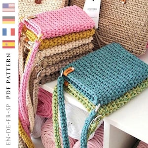 Op de afbeelding: Een verzameling handgemaakte gehaakte tassen in verschillende kleuren, waaronder roze, geel en blauwgroen. De tassen hebben lange banden en worden op een witte plank getoond. De afbeelding bevat ook een label met "ANDREAM".