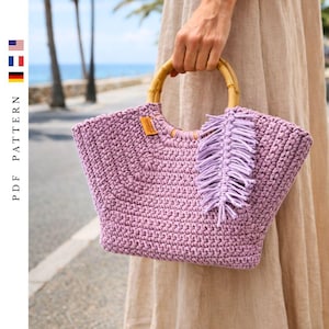 May include: A lavender crochet tote bag with a bamboo handle and a fringe detail. The bag has a rectangular shape and a small tag. The text "PDF PATTERN" is printed vertically on the left side of the image.