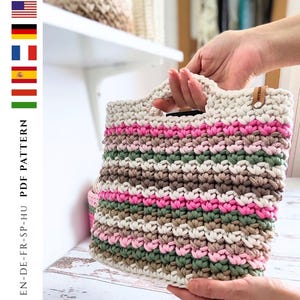 Puede incluir: Un bolso tote de ganchillo con un diseño a rayas en crema, rosa, marrón y verde. El bolso tiene forma rectangular con un asa y una pequeña etiqueta de cuero. El texto "PDF PATTERN" es visible en el lateral.