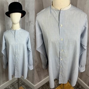 Pu&ograve; includere: Una camicia a maniche lunghe a righe blu chiaro con colletto alla coreana e chiusura con bottoni. La camicia ha un bordo bianco intorno al colletto.