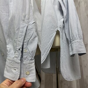 Pu&ograve; includere: Una camicia a maniche lunghe a righe blu chiaro e bianche con colletto abbottonato e polsino con un bottone. La camicia ha uno spacco laterale ed &egrave; realizzata in un tessuto leggero.