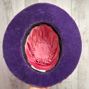 May include: A purple velvet hat with a pink satin lining. The hat has a wide brim and a rounded crown.