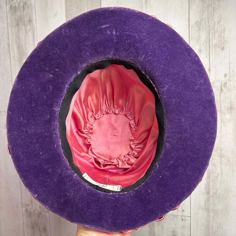 May include: A purple velvet hat with a pink satin lining. The hat has a wide brim and a rounded crown.