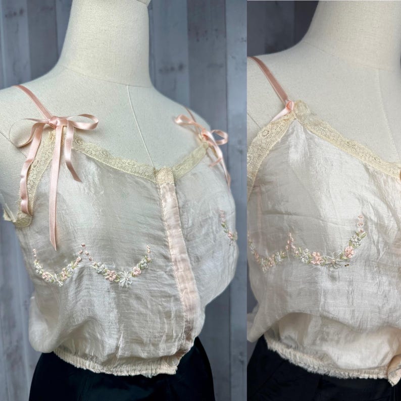 May include: A delicate, sheer, blush-colored camisole with delicate floral embroidery and satin ribbon straps. The camisole has a button-up front and a gathered hem.