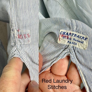 Pu&ograve; includere: Primo piano di una camicia a righe blu e bianche con cuciture rosse. La camicia ha un'etichetta che recita "CHARTRAIRE 37, Rue Marbeuf PARIS".