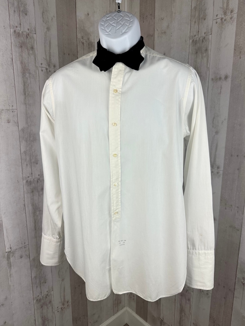Pu&ograve; includere: Una camicia bianca a maniche lunghe con bottoni e un colletto a farfalla nero. La camicia ha una singola patta con bottoni e un piccolo cartellino in basso a sinistra che recita "Made in the USA".