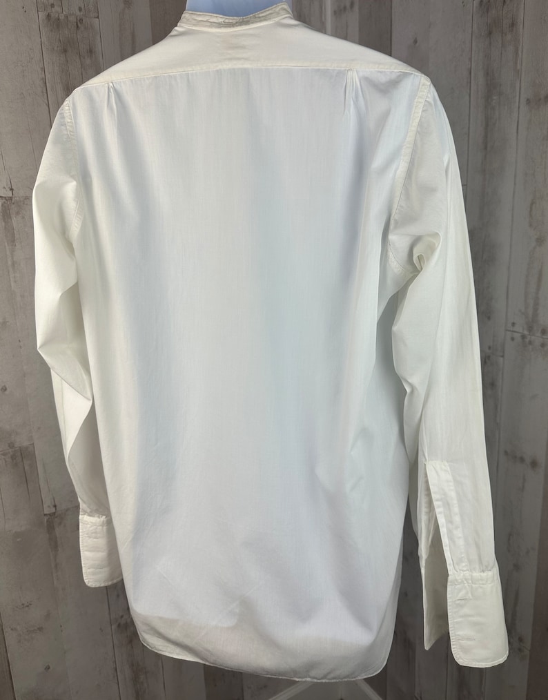 Pu&ograve; includere: Una camicia bianca a maniche lunghe con colletto alla coreana e polsini doppi.