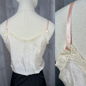 May include: A white satin camisole with delicate lace trim and thin pink straps. The camisole is worn on a white mannequin.