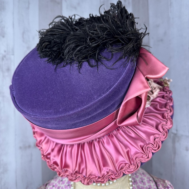 May include: A purple velvet hat with a pink satin ruffle and a black feather trim.