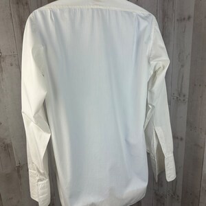 Pu&ograve; includere: Una camicia bianca a maniche lunghe con bottoni e colletto alla coreana. La camicia &egrave; appesa a un appendiabiti.