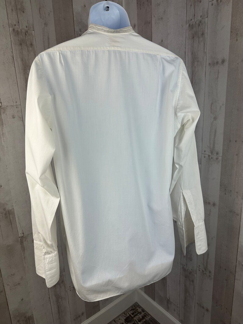 Pu&ograve; includere: Una camicia bianca a maniche lunghe con bottoni e colletto alla coreana. La camicia &egrave; appesa a un appendiabiti.