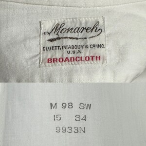 Pu&ograve; includere: Camicia bianca con un'etichetta del marchio Monarch, che presenta il testo "CLUETT, PEABODY & CO INC. U.S.A. BROADCLOTH". L'etichetta di taglia della camicia riporta "M 98 SW 15 34 9933N".