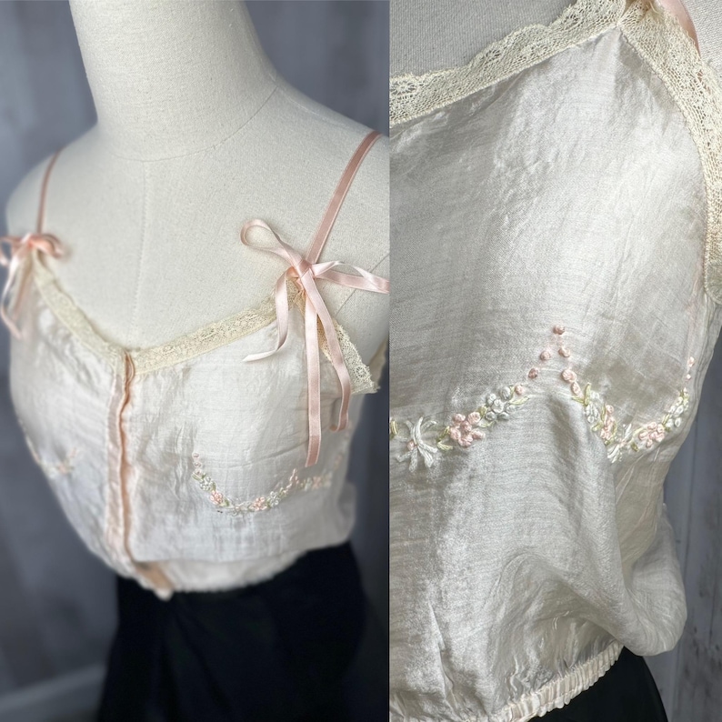 May include: A delicate, pale pink silk camisole with delicate floral embroidery and lace trim. The straps are tied with bows.