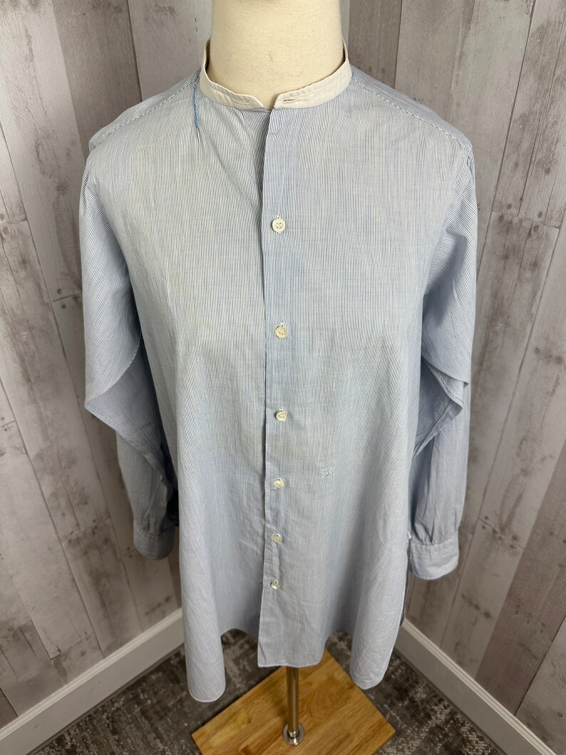 Pu&ograve; includere: Una camicia a maniche lunghe a righe blu chiaro con colletto alla coreana bianco e chiusura con bottoni.