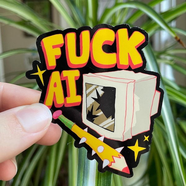 May include: A sticker with the words "FUCK AT" in yellow letters with a red outline, set against a black background. The sticker features a cartoon image of a broken computer monitor and a yellow pencil with white spikes.